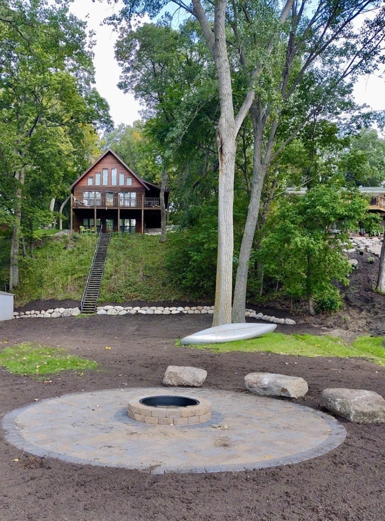 fire pit surrounded by trees and greenery with a house on a hill overlooking it